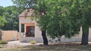 Un edificio de una sola planta con techo de tejas, un área de estar al aire libre cubierta y un árbol en primer plano.