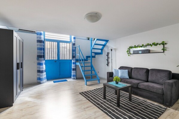 A living room with a sofa, a coffee table, a staircase, and a door leading to another room.