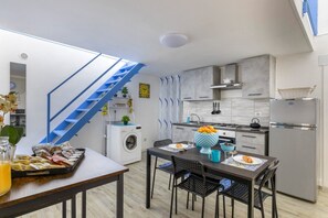 A compact kitchen with a washing machine, a dining area with a table and chairs, and a blue staircase.