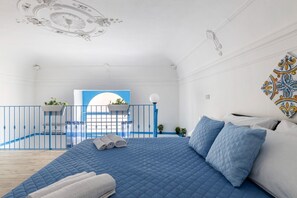 A bedroom with a large bed, a balcony with a railing, and a view of the sea.