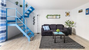 Ett modernt vardagsrum med en blå trappa, en mörk soffa, ett litet soffbord och en svartvit randig matta.