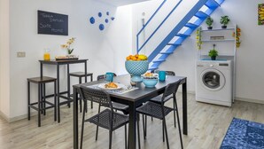Ett kompakt bostadsutrymme med en matplats, en tvättmaskin, en trappa och en tavla som används som anslagstavla.