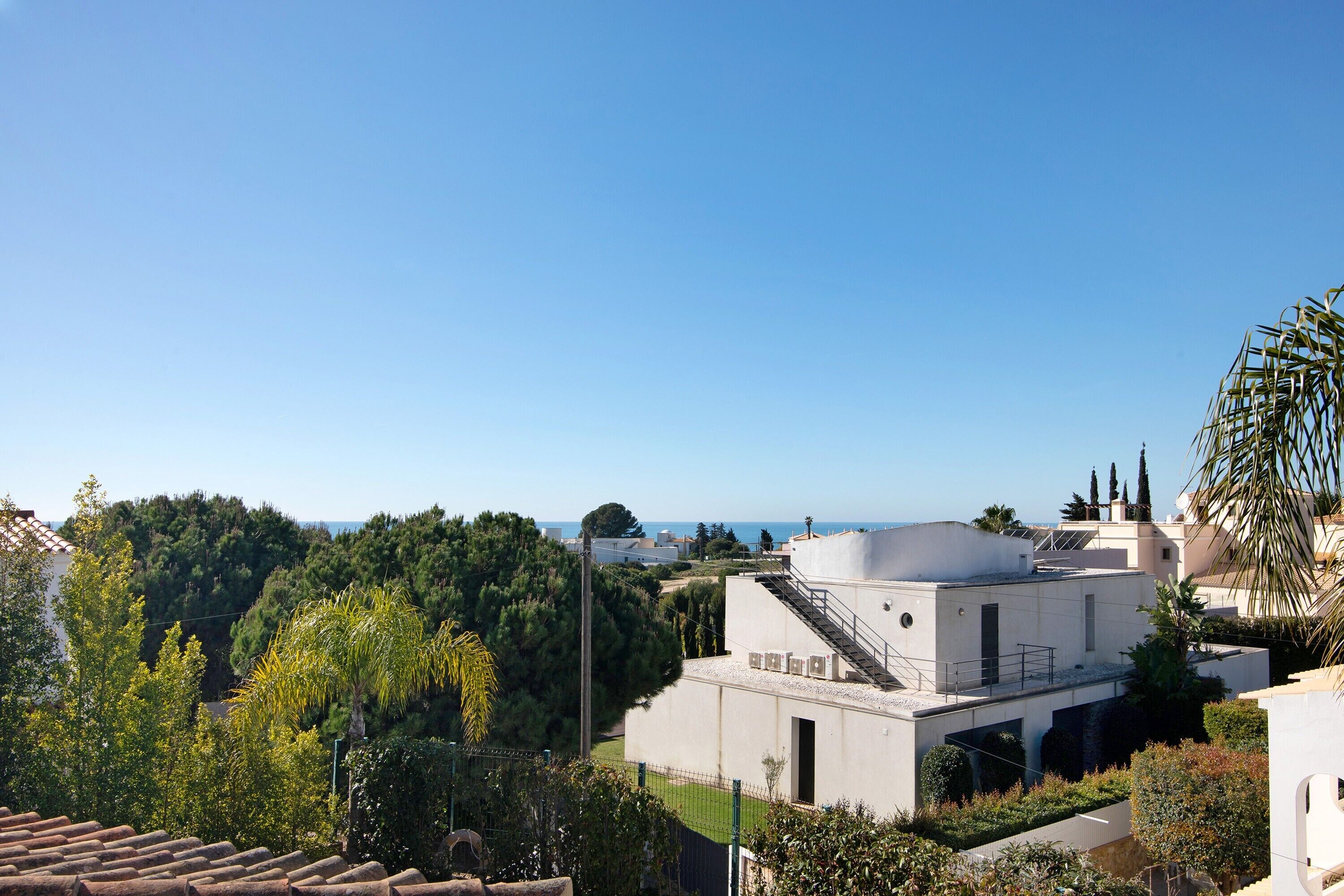 A modern building with a flat roof, surrounded by greenery and a clear sky.
