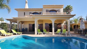 A pool with lounge chairs, a covered patio, and a building with arches and a tower.