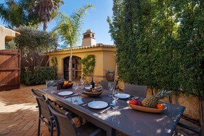 An outdoor dining area with a table set for two, surrounded by chairs, a bowl of fruit, and wine glasses. - Villa 'Rústica' with Sea View, Wi-Fi and Air Conditioning (Albufeira)
