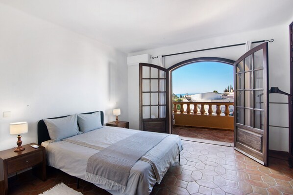 A bedroom with a bed, nightstands, a view of a balcony, and a large arched window.