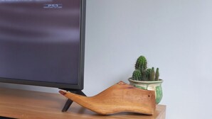 A wooden TV stand with a flat-screen TV displaying a date and time. A wooden tray rests on the stand, and a small potted cactus is visible in the background. - 20 minutes from Rosario! Ideal house to disconnect from the routine.  (Santa Fe)