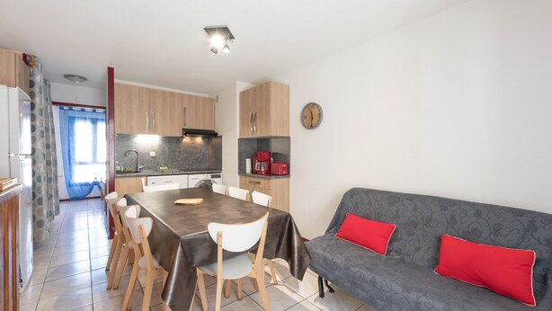 A modern kitchen with a dining area, a sofa with red cushions, and a clock on the wall.