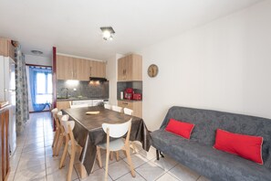 A modern kitchen with a dining area, a sofa with red cushions, and a clock on the wall. - Gavarnie Apartment – Comfortable Duplex with Parking & Ski Locker (Gavarnie-Gèdre)