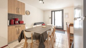 A dining area with a table, chairs, a clock, and a refrigerator.