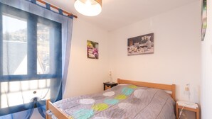A bedroom with a bed, a nightstand, a lamp, a window with curtains, and two wall-mounted pictures.
