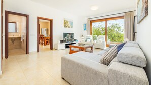 A living room with a sofa, television, dining area, and large windows.