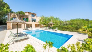 A swimming pool with lounge chairs, a building with a balcony, and surrounding greenery.