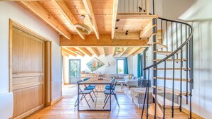 A spacious room with a wooden floor, a dining area with a table and chairs, a sofa, and a staircase with a metal railing.