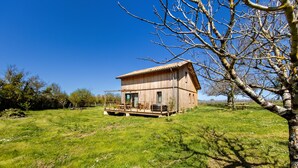A rustic wooden house with a porch, surrounded by a grassy field and trees.