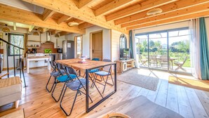 A spacious wooden interior with a dining area, kitchen, and large windows.