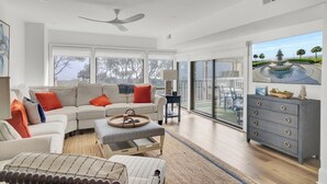 A spacious living room with a large sofa, a coffee table, and a view of a fountain through large windows. - Award-Winning Resort Amenities | Ocean Club 4102 (Isle of Palms)