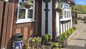 A traditional Tudor-style building with white and dark brown timber framing, a brick chimney, and hanging flower baskets. - The Fighting Cocks  (Fordingbridge)