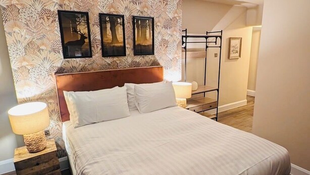 A neatly made bed with a headboard, two bedside tables with lamps, and a patterned wallpaper. - The Fighting Cocks  (Fordingbridge)