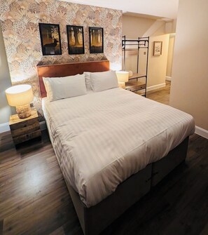Una cama bien hecha con cabecera, dos mesitas de noche con lámparas y un papel tapiz estampado.