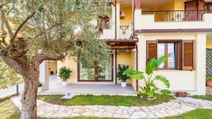 A two-story building with a stone pathway, potted plants, and a large tree. - Holiday Home 'Laura' with Private Terrace, Wi-Fi and Air Conditioning (Bari Sardo)