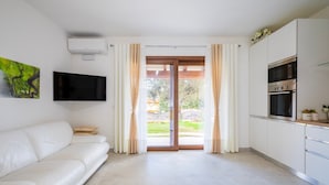 A modern living room with a white sofa, a flat-screen TV, and a sliding glass door leading to a balcony. - Holiday Home 'Laura' with Private Terrace, Wi-Fi and Air Conditioning (Bari Sardo)