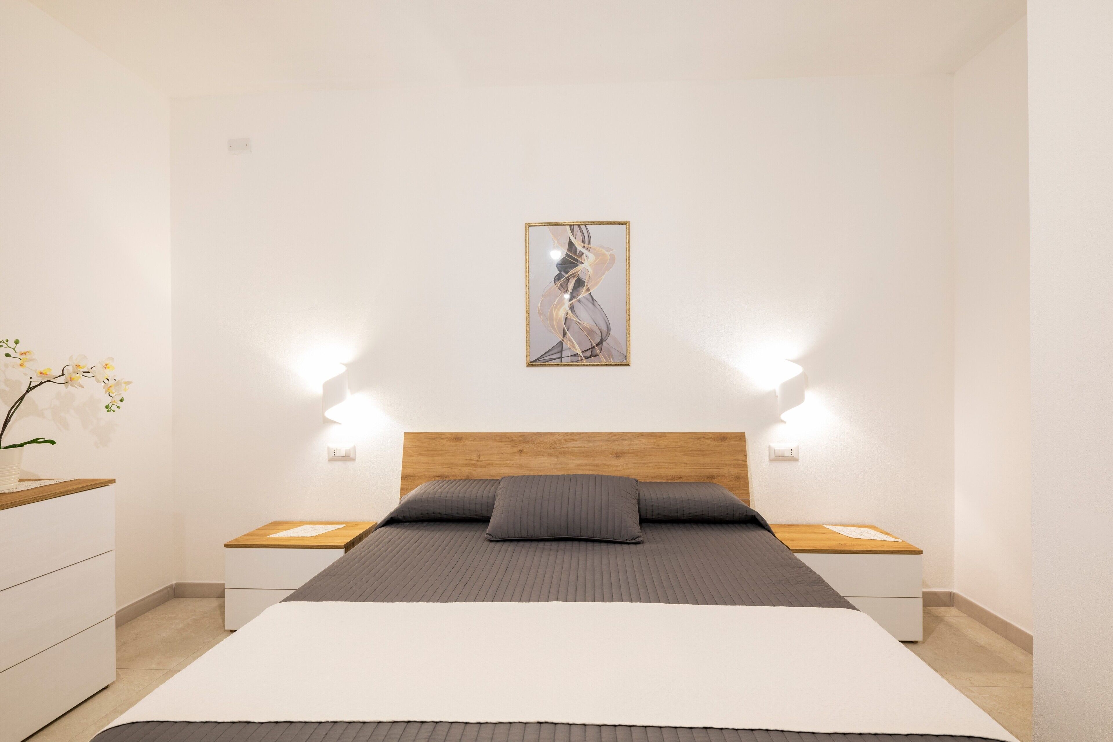 Ein Schlafzimmer mit einem Bett, Nachttischen, einer Wanddekoration und einer Vase mit Blumen.