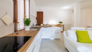 A modern kitchen with a central island, white cabinetry, and a dining area with a white sofa and a green pillow. - Holiday Home 'Laura' with Private Terrace, Wi-Fi and Air Conditioning (Bari Sardo)