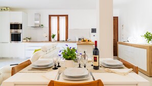 A modern kitchen with white cabinetry, a dining area with a table set for four, and a visible wine bottle. - Holiday Home 'Laura' with Private Terrace, Wi-Fi and Air Conditioning (Bari Sardo)