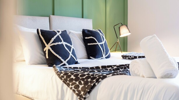 A neatly made bed with white and patterned bedding, a green headboard, and a lamp on the side. - The Annick Suite No.2 (Irvine)