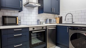 A modern kitchen with dark blue cabinets, a microwave, oven, dishwasher, and a sink with a faucet. - The Annick Suite No.2 (Irvine)