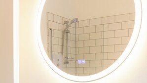 A bathroom with a round mirror, white sink, and two black cups on the counter. - The Annick Suite No.2 (Irvine)