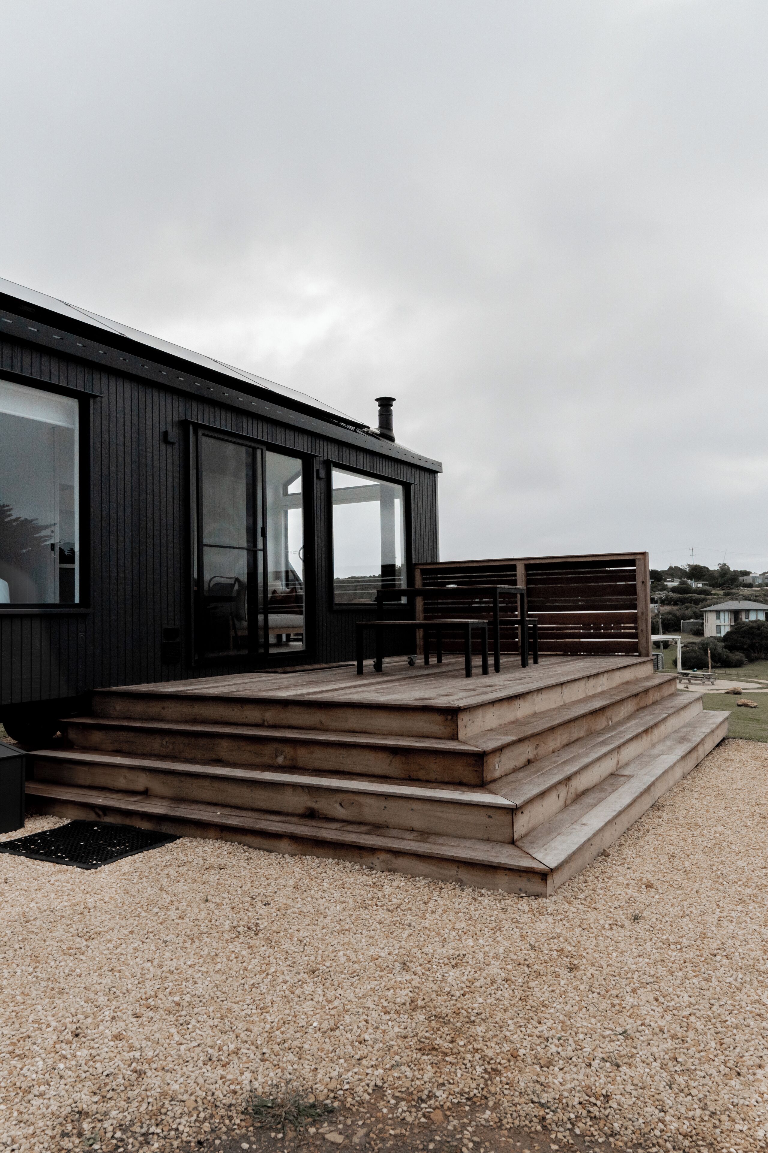 Un edificio moderno con una terrazza in legno, ampie finestre e un terreno in ghiaia.