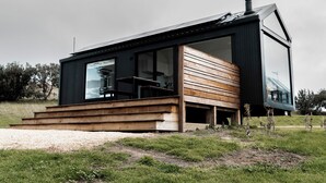Una casa moderna con un amplio ventanal, terraza de madera y fachada negra.