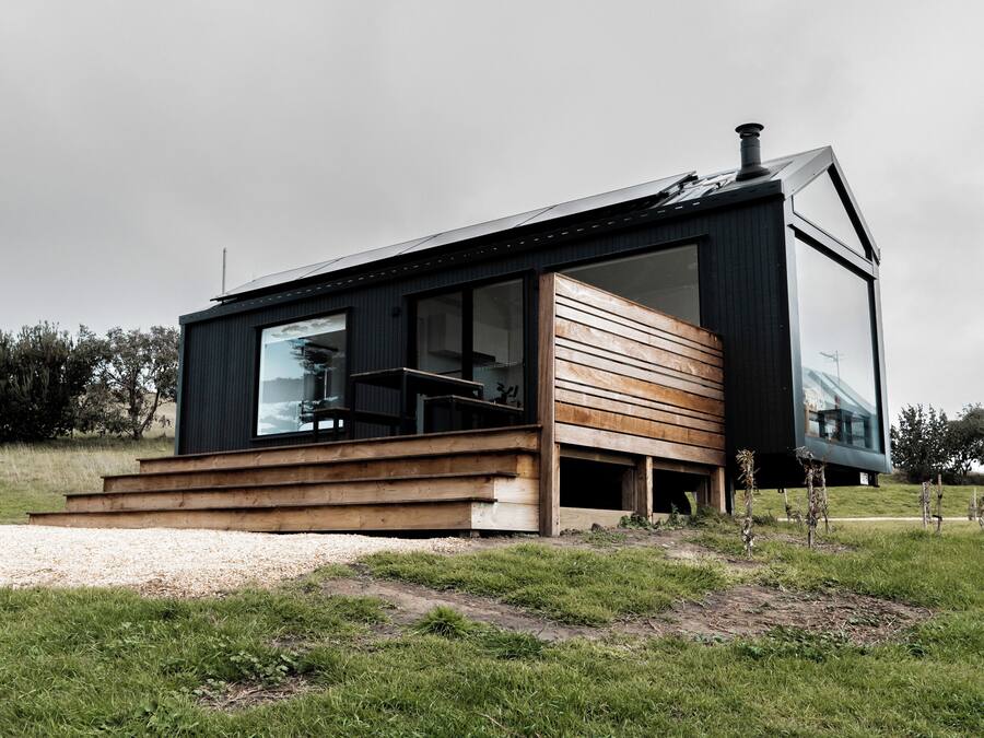 Uma casa moderna com uma ampla janela de vidro, deck de madeira e fachada preta.