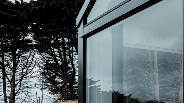Una casa moderna con un amplio ventanal, una terraza de madera y vista al océano.