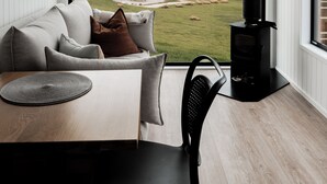 Una sala de estar moderna con un ventanal grande, una estufa de leña negra, una mesa de madera y un sofá con cojines.