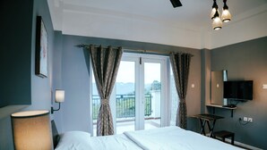 Ein Schlafzimmer mit Bett, Nachttischlampe, Fernseher und einem Balkon mit Vorhängen.