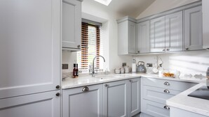 A modern kitchen with white cabinets, a skylight, and a countertop with various kitchen items. - Shepherd's Cottage -  a beautiful cottage sleeping 2 guests (Usk)