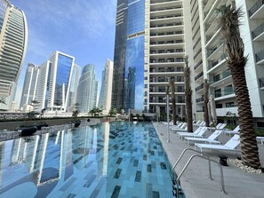 A swimming pool with lounge chairs and palm trees, surrounded by high-rise buildings.