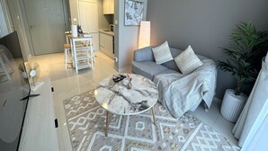 A modern living room with a grey sofa, a coffee table, and a kitchen in the background. - Easygo-cozy 1bdr Zada Tower (Dubai)