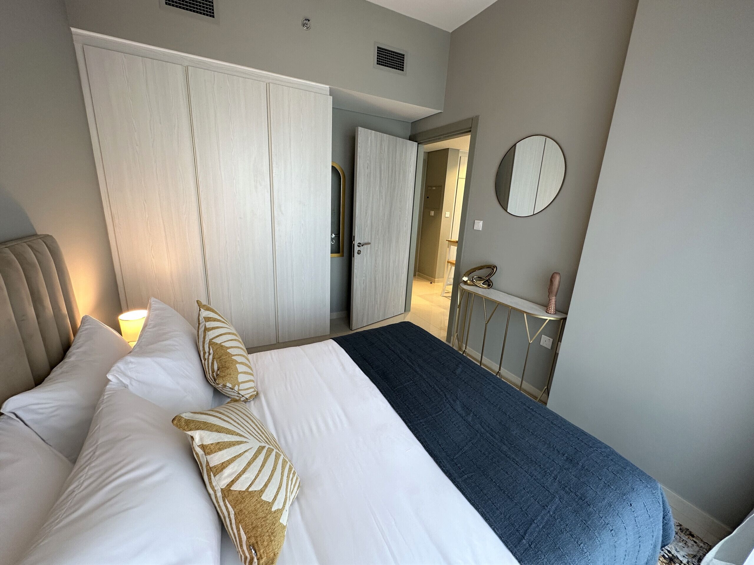 Un dormitorio con cama, almohadas, mesita de noche, espejo y armario.