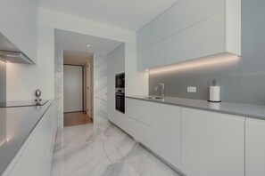 Una cocina moderna con armarios blancos, suelo de mármol y electrodomésticos integrados.