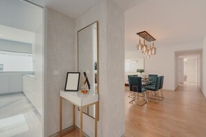 Un interior moderno con un escritorio blanco, un espejo grande, y una zona de comedor con sillas color turquesa y una araña.