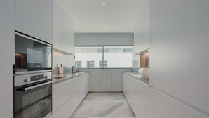 A modern kitchen with white cabinetry, a built-in oven, and a large window providing natural light. - Apartment 'Lux In Porto' with Wi-Fi and Air Conditioning (Porto)