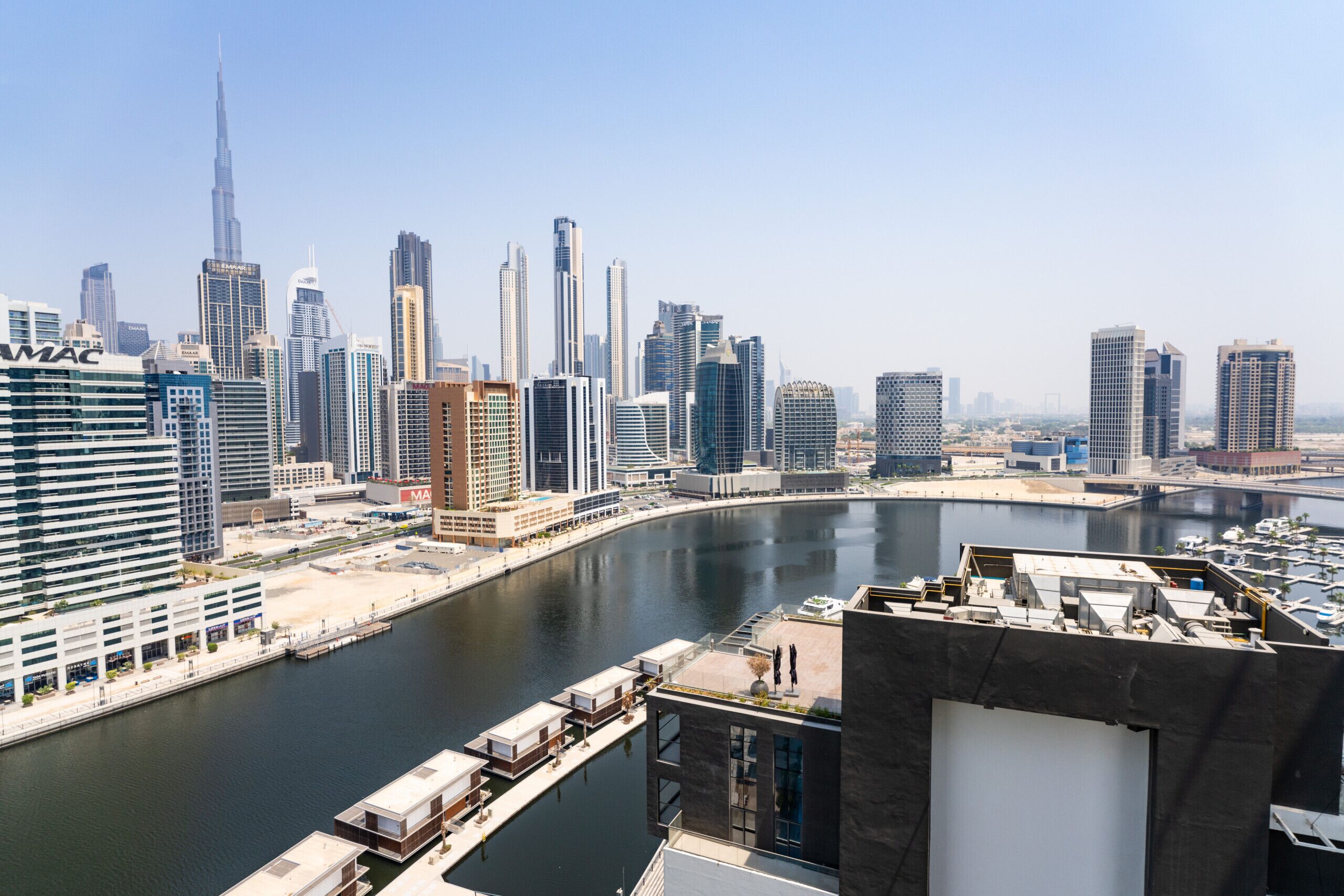 A high-rise building with a river in the foreground and a city skyline in the background.