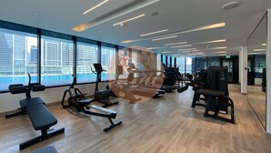 A modern gym with exercise equipment, large windows, and a view of the city. - Easygo- Luxury 1bdr With View Bin Can (Dubai)