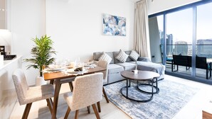 A modern living room with a dining area, a sofa, and a large window with a city view. - Easygo- Luxury 1bdr With View Bin Can (Dubai)