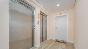 Un corridoio con due ascensori, una porta bianca e un pavimento in legno.