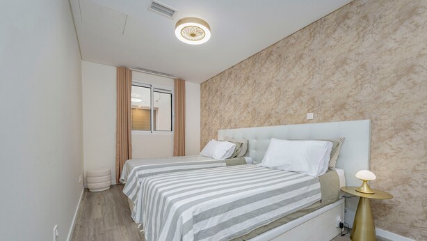 Una camera da letto moderna con due letti, una finestra, un comodino con una lampada e una parete decorata.